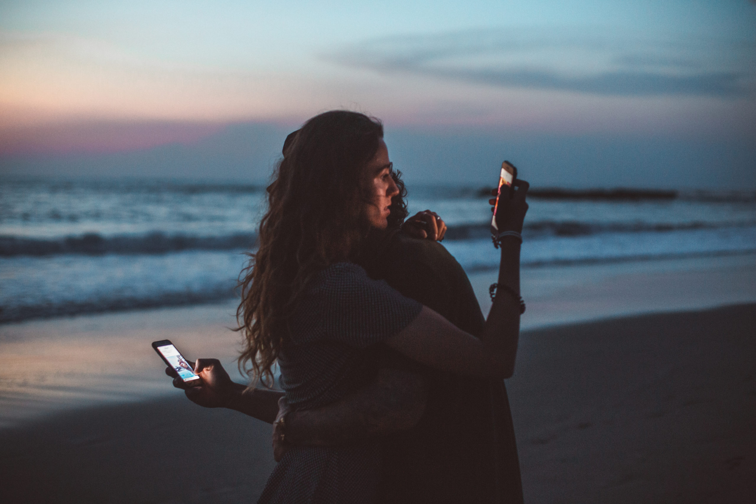 couple-hugging-and-using-smartphone-near-sea-on-sunset-4555321